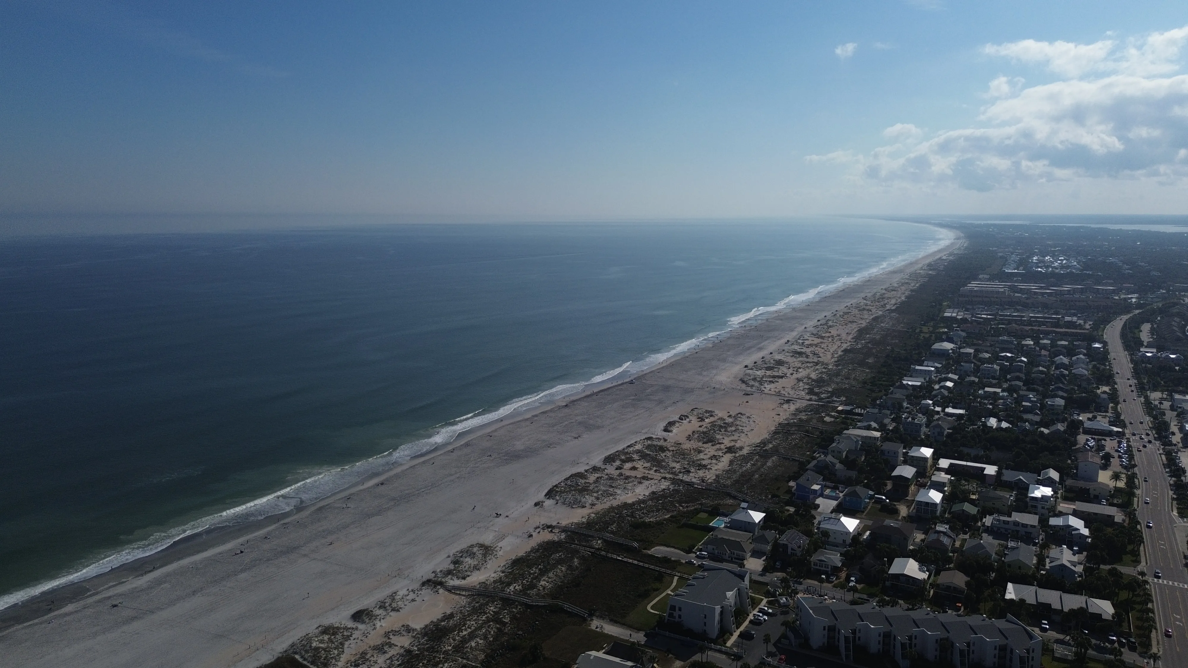 Long sandy shoreline and ocean seen from above on a bright day.
